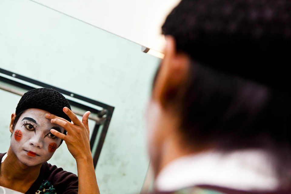 A theatre performer applies makeup in a mirror