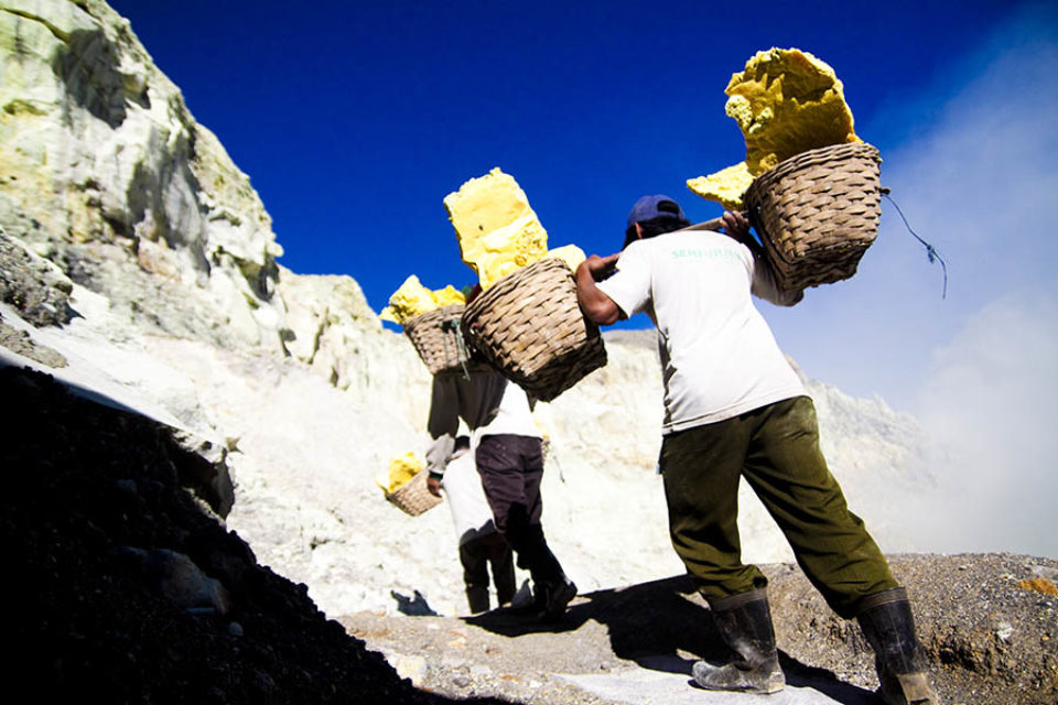 Miners carrying baskets of sulphur out of the mine