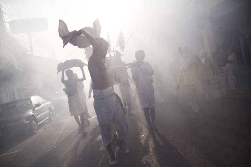 Litter bearers walk through firecracker smoke