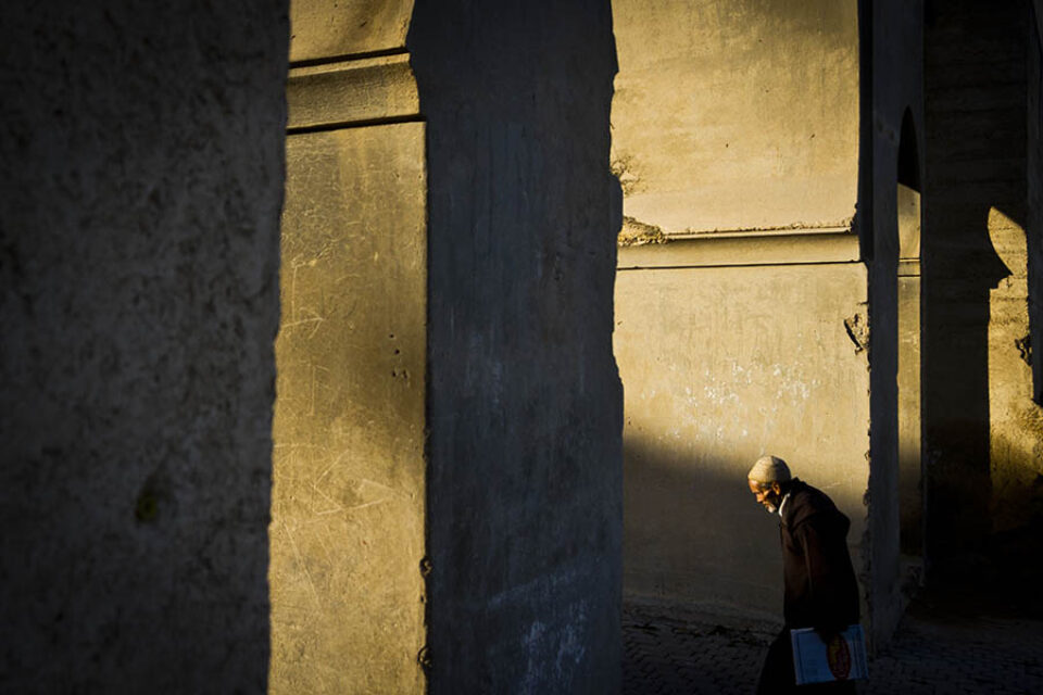 Man walks through sunlit arches Fez, Morocco